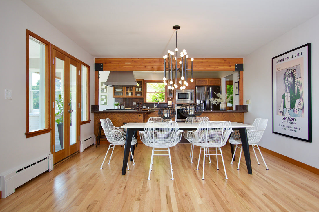 Dining table with white chairs, an adjoining kitchen and contemporary artwork.