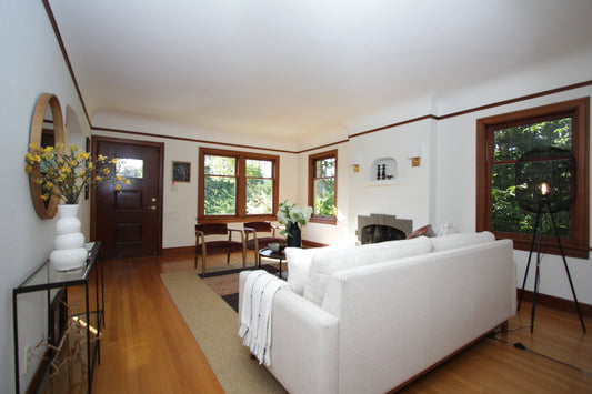 Queen Anne living room with pale sofa, dark wood trim, fireplace and wood-framed windows.