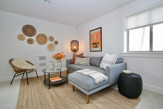 Living room staged with a gray sectional, woven chair, rug and artwork.