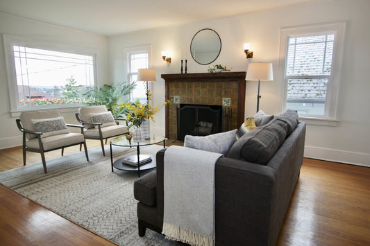Staged living room with a gray sofa, two light armchairs and a tile fireplace.