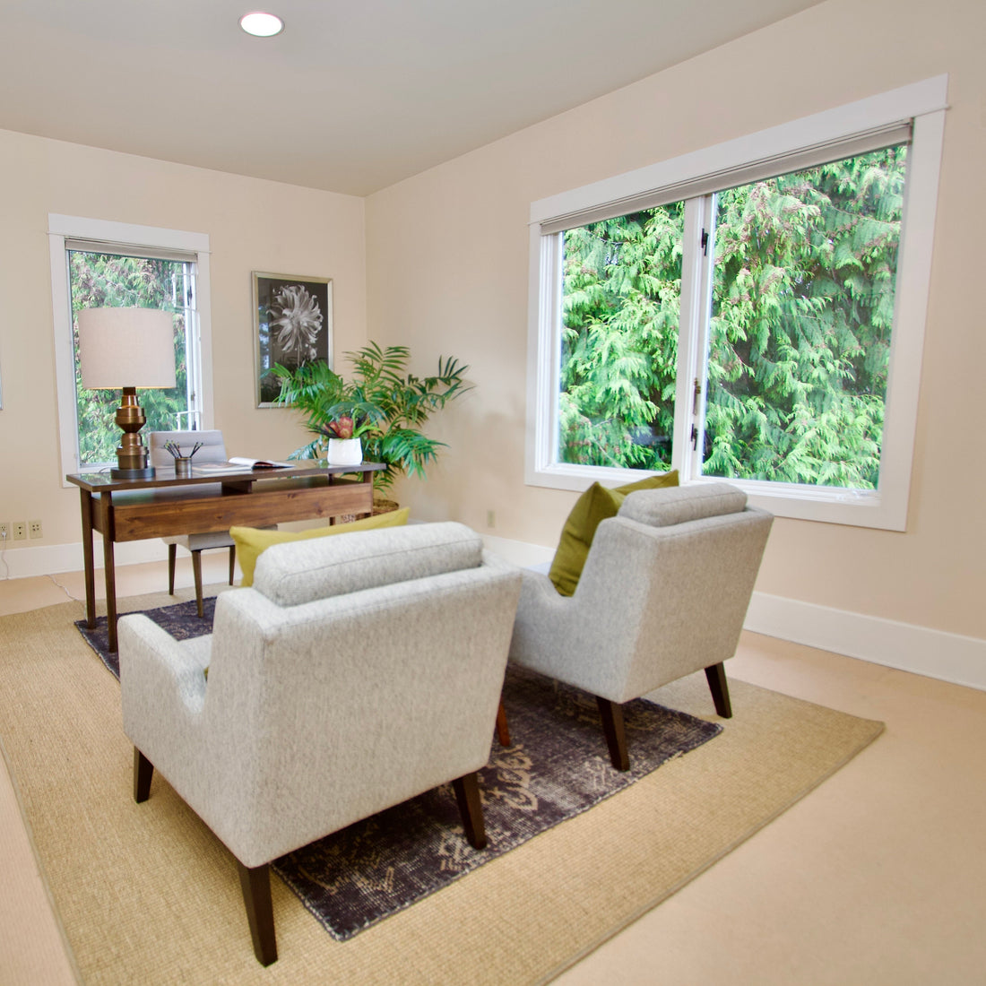 Two pale lounge chairs facing a desk in a bright room with garden views.