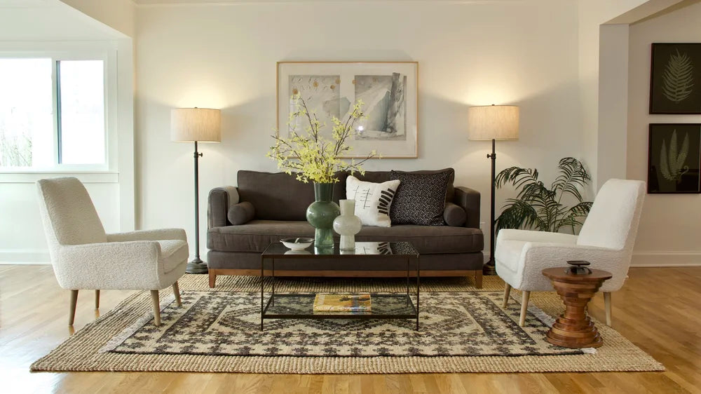 A charcoal sofa and pale chairs with layered rugs and flowering branches, staged by Nob Hill Style.